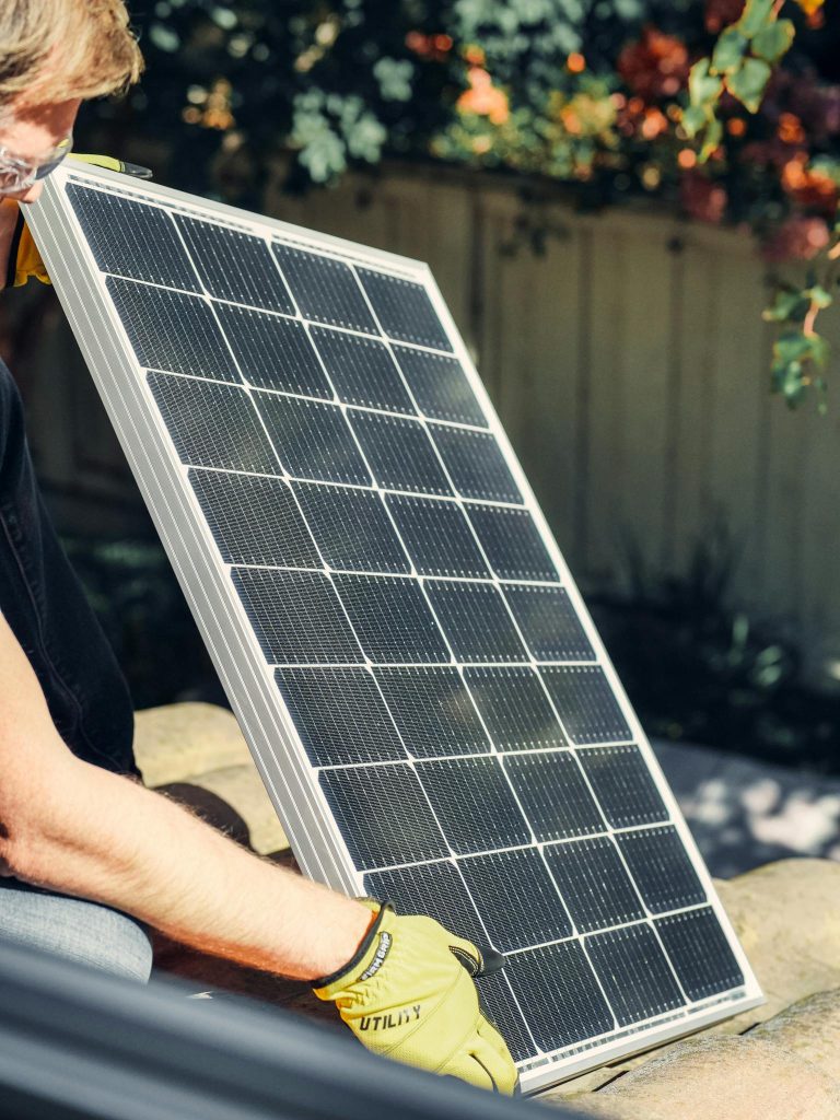 A worker installs a solar panel in a garden, promoting clean energy.